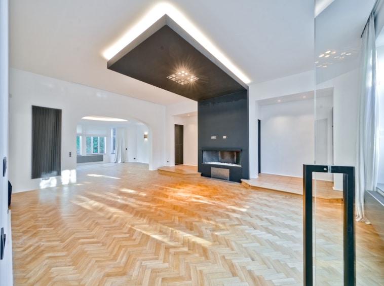 Salon moderne lumineux avec parquet en chevrons, cheminée design et grandes fenêtres.