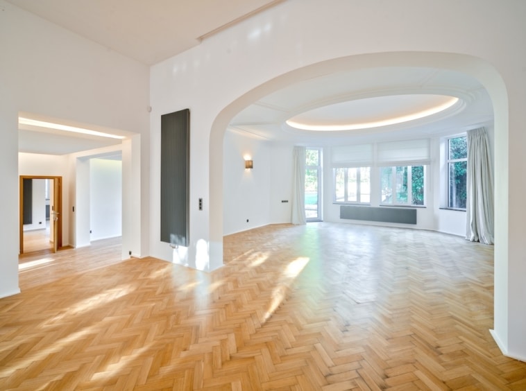 Salon lumineux avec plafond courbe, murs blancs, sol en chevrons et espace cosy intégré.