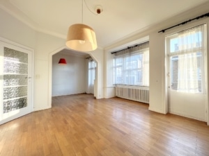 Salon lumineux avec grandes fenêtres, parquet en bois, plafond haut et décoration minimaliste élégante.