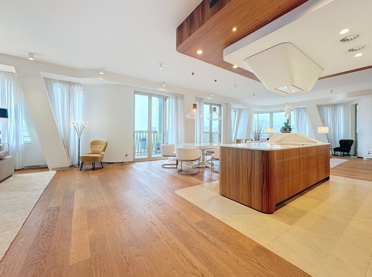 Salon moderne lumineux avec cuisine ouverte en bois, grand canapé, mobilier minimaliste et vue extérieure.