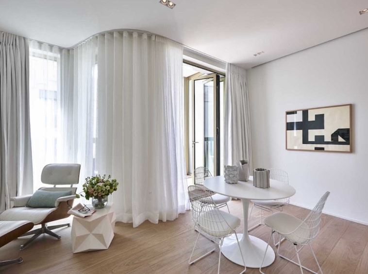 Salon minimaliste lumineux avec mobilier moderne, art abstrait, fenêtres en sheer blanc, ambiance élégante.