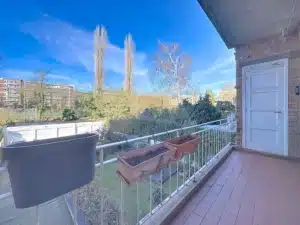 Balcon paisible avec vue sur jardin verdoyant, arbres nus, ciel bleu, et buildings résidentiels.