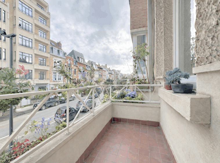 Balcon avec vue sur rue urbaine animée, plantes en pot et atmosphère paisible.