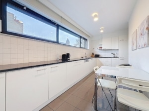 Cuisine moderne lumineuse avec mobilier minimaliste, grandes fenêtres, coin repas élégant et appareils intégrés.