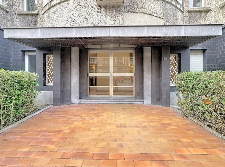Entrée moderne avec façade en béton, fenêtres géométriques et jardin soigneusement aménagé.