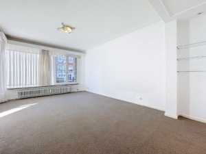 Salon lumineux avec vue urbaine murs blancs grandes fenêtres sol beige étagères en verre