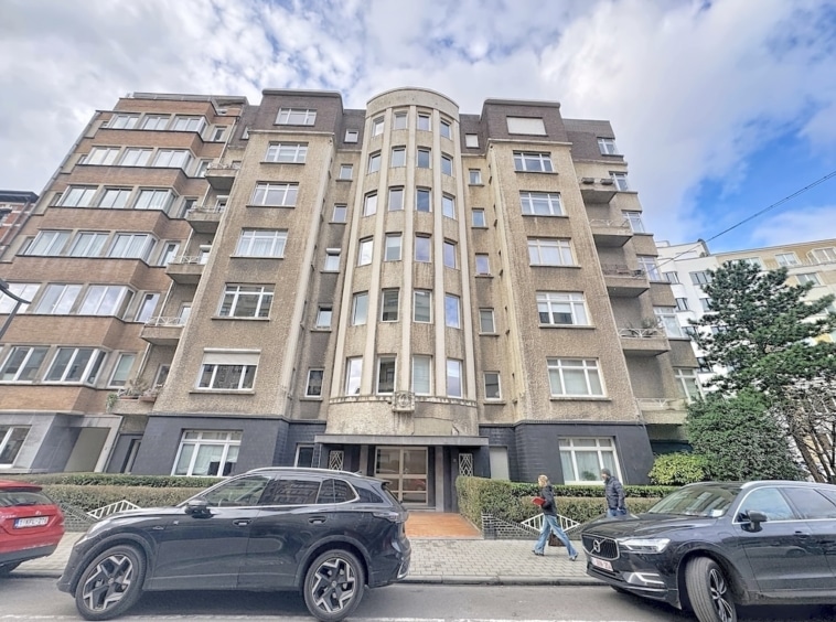 Immeuble résidentiel Art Déco avec tour arrondie, façade en brique, fenêtres élégantes, rue animée.