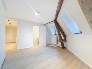 Loft lumineux avec poutres en bois murs blancs fenêtres inclinées et plancher en bois clair