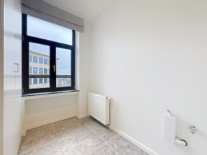Studio lumineux avec grande fenêtre, vue urbaine, décoration minimaliste et coin plomberie dissimulé.