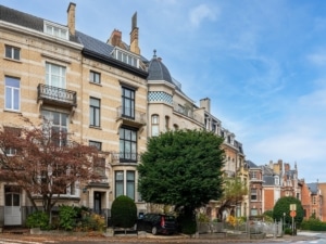 Rue résidentielle charmante avec bâtiments en briques, végétation luxuriante et ciel ensoleillé.