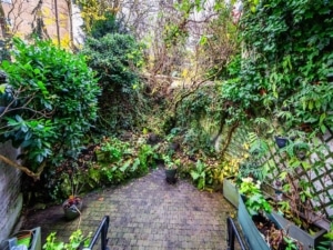 Jardin secret sauvage, chemin en briques, murs recouverts de lierre, ambiance paisible et mystérieuse.