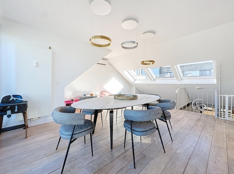 Salle à manger moderne lumineuse avec table ronde, chaises grises et éclairage design minimaliste.