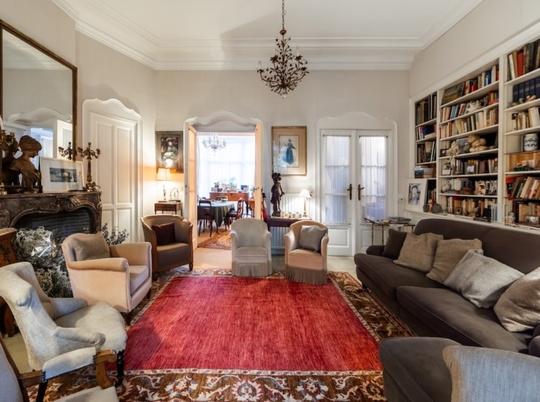 Salon cosy et élégant avec bibliothèque, chandelier, fauteuils lumineux et ambiance chaleureuse.