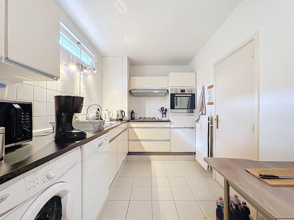Moderne witte keuken met zwart werkblad, geïntegreerde apparatuur, licht en functioneel.