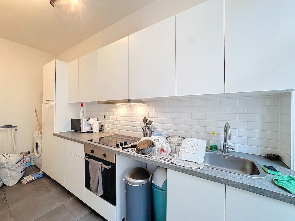 Cuisine moderne lumineuse à Lyon, avec mobilier blanc, carrelage subway, et espace utilitaire organisé.