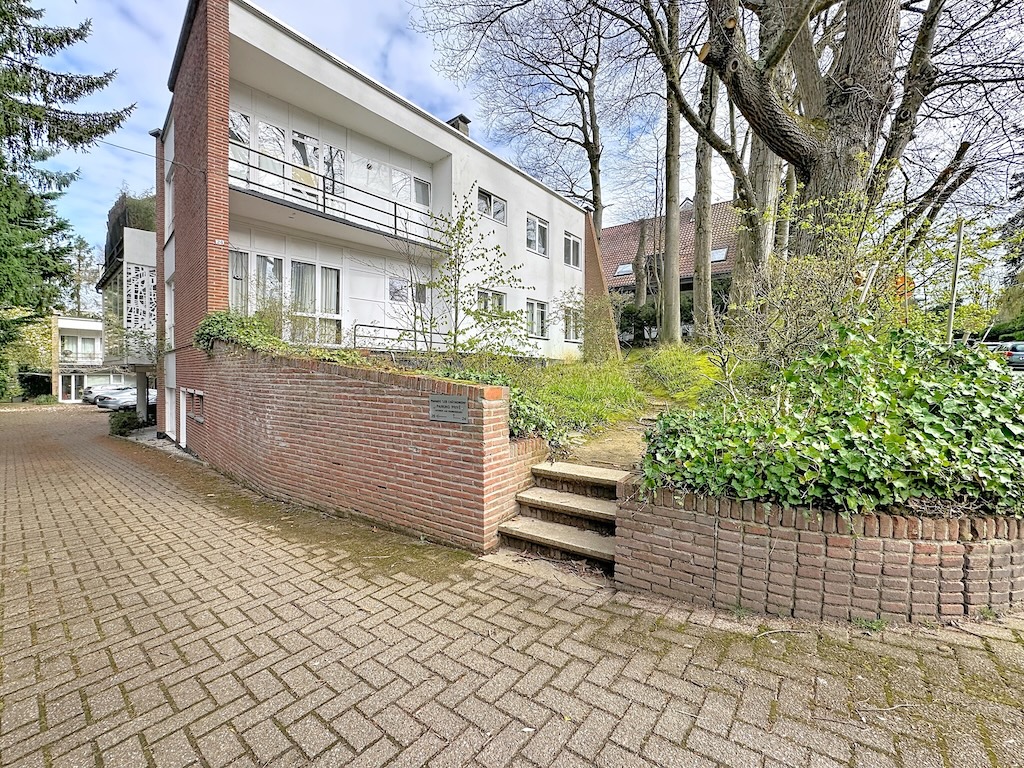 Moderne gevel van wit woongebouw met balkons, ronde tuin, kale bomen, in [Locatie].