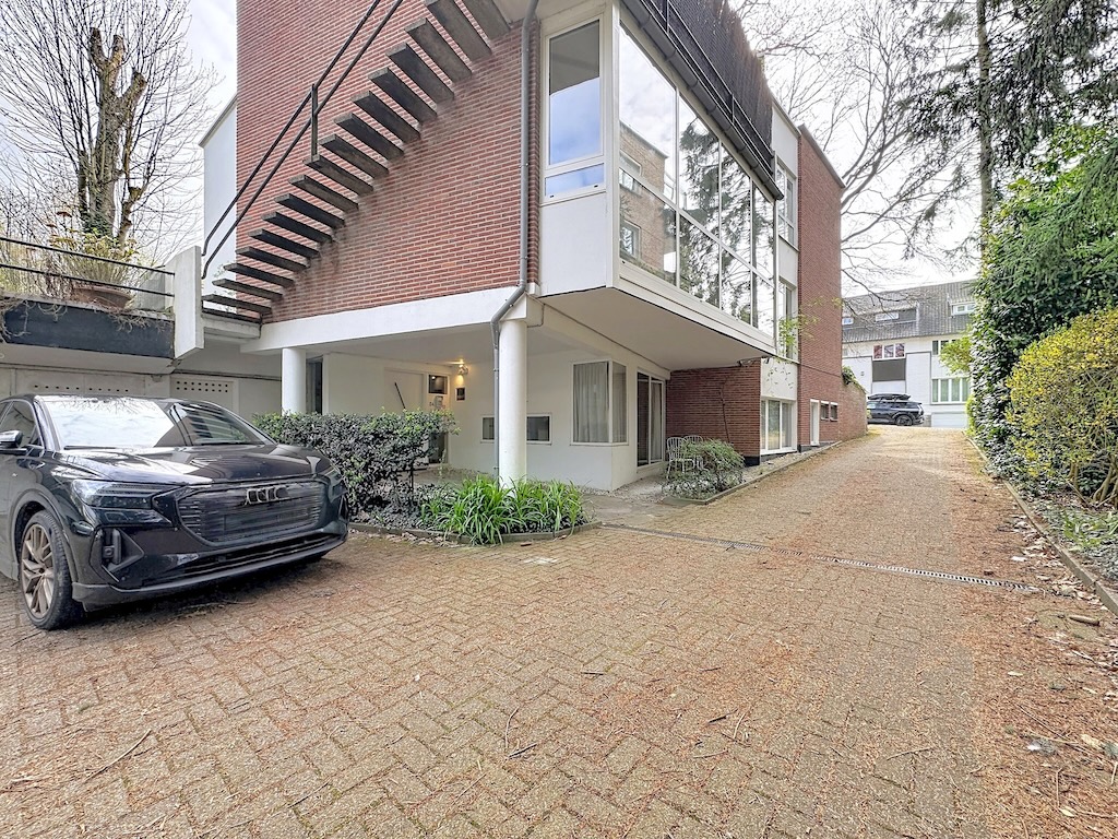 Moderne gevel in Ukkel met parkeerplaats, grote ramen en verzorgde tuin.