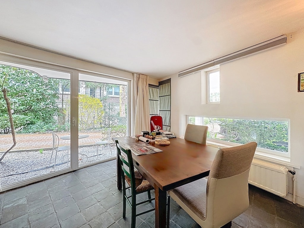 Lichte eetkamer met houten tafel, eclectische stoelen, groen uitzicht in Ukkel.