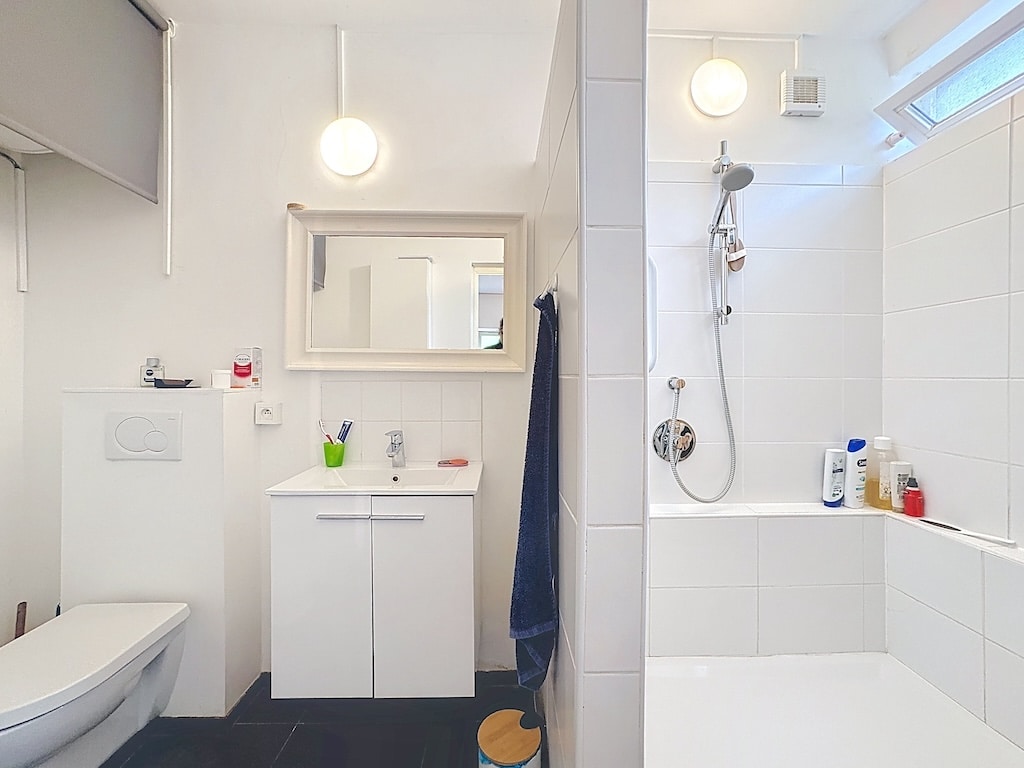 Lichte, moderne badkamer in Ukkel met minimalistisch wit meubilair en wit betegelde douche.