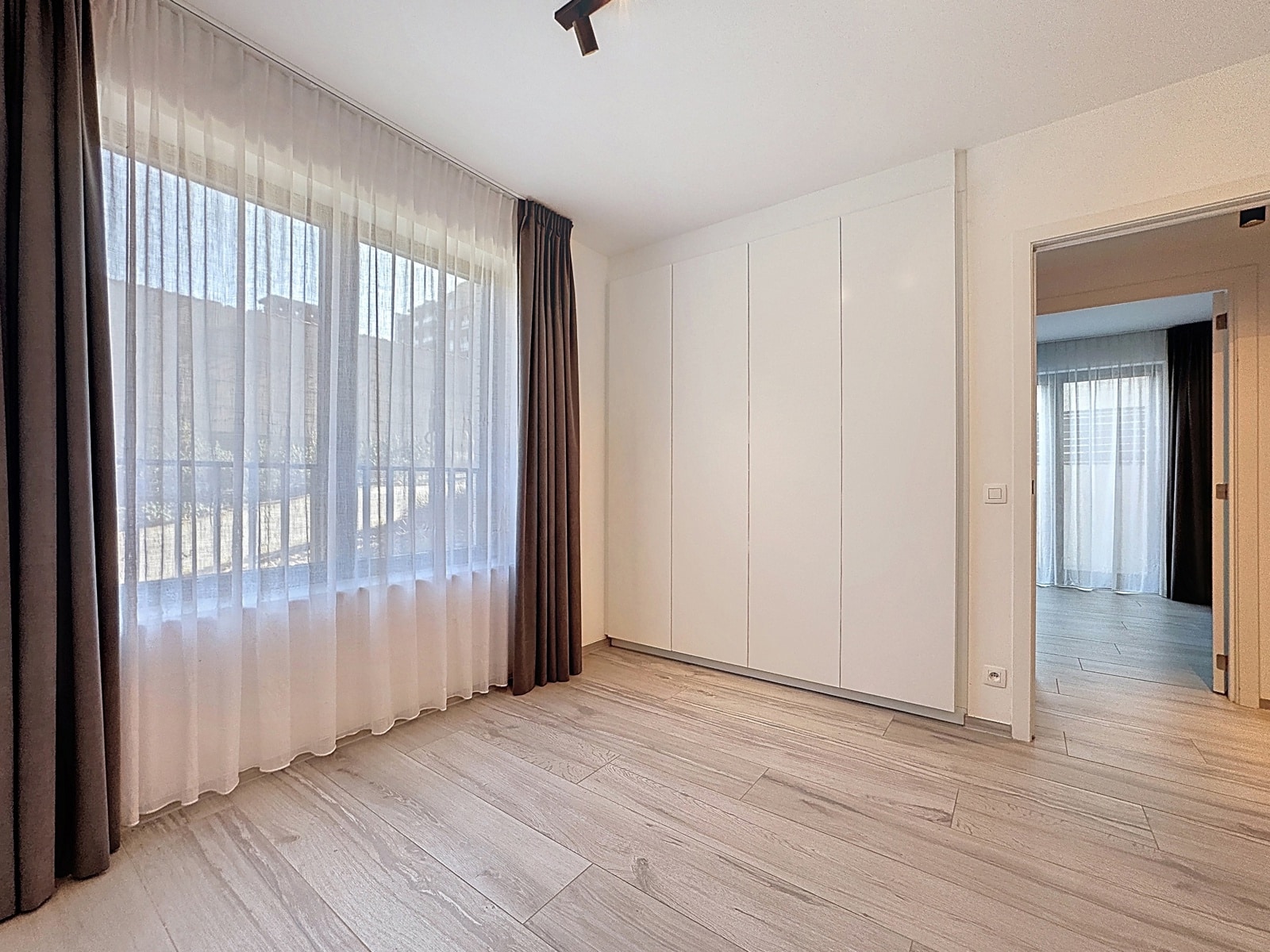 Chambre Lumineuse avec Placards – You Real Estate Agency Chambre lumineuse avec placards intégrés, parquet clair et grande fenêtre voilée
