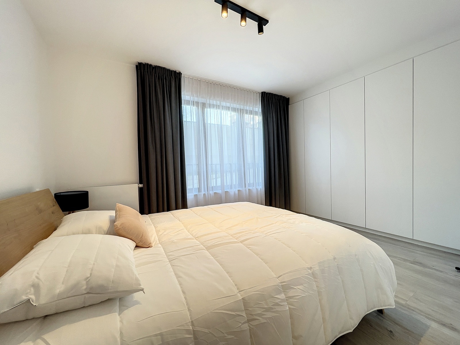 Chambre Moderne avec Lit Blanc – You Real Estate Agency Chambre moderne lumineuse avec lit blanc, placards intégrés et rideaux gris.
