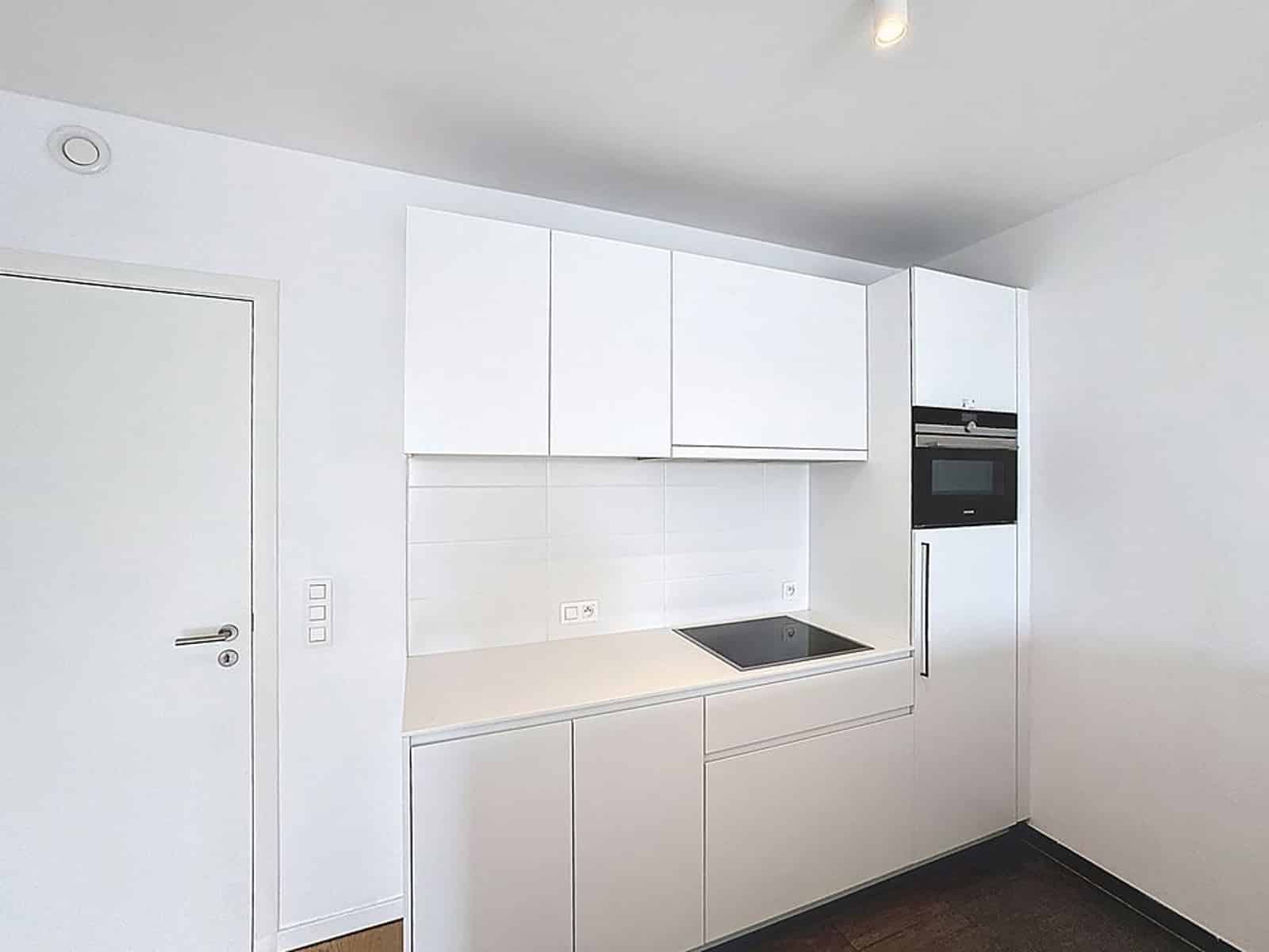 White kitchen with built-in oven - You Real Estate Agency Modern white kitchen with integrated oven, induction hob and minimalist storage units