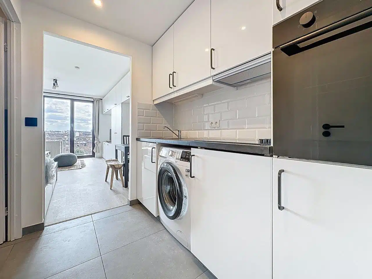 Studio White Kitchen - You Real Estate Agency Modern white kitchen in a studio apartment overlooking a bright living room.