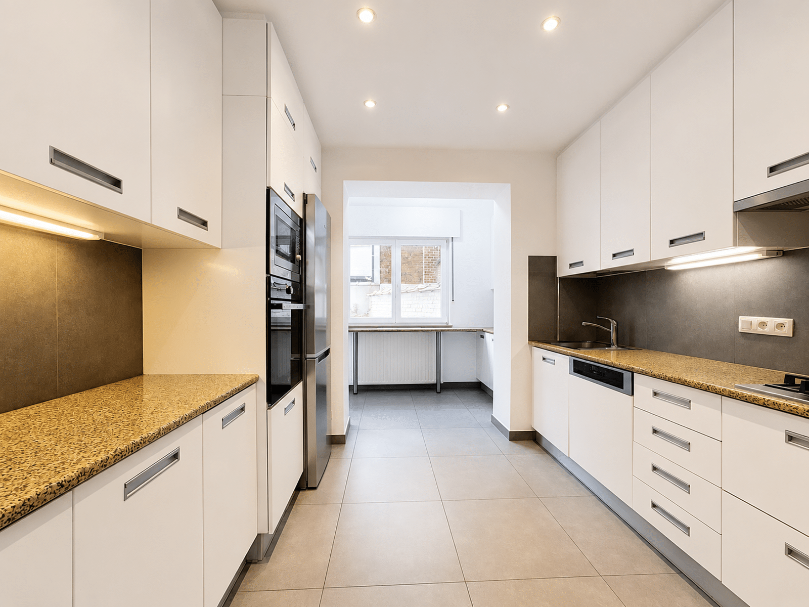 Bright fitted kitchen in corridor - You Real Estate Agency Bright, modern fitted kitchen in hallway with white cabinetry and integrated appliances