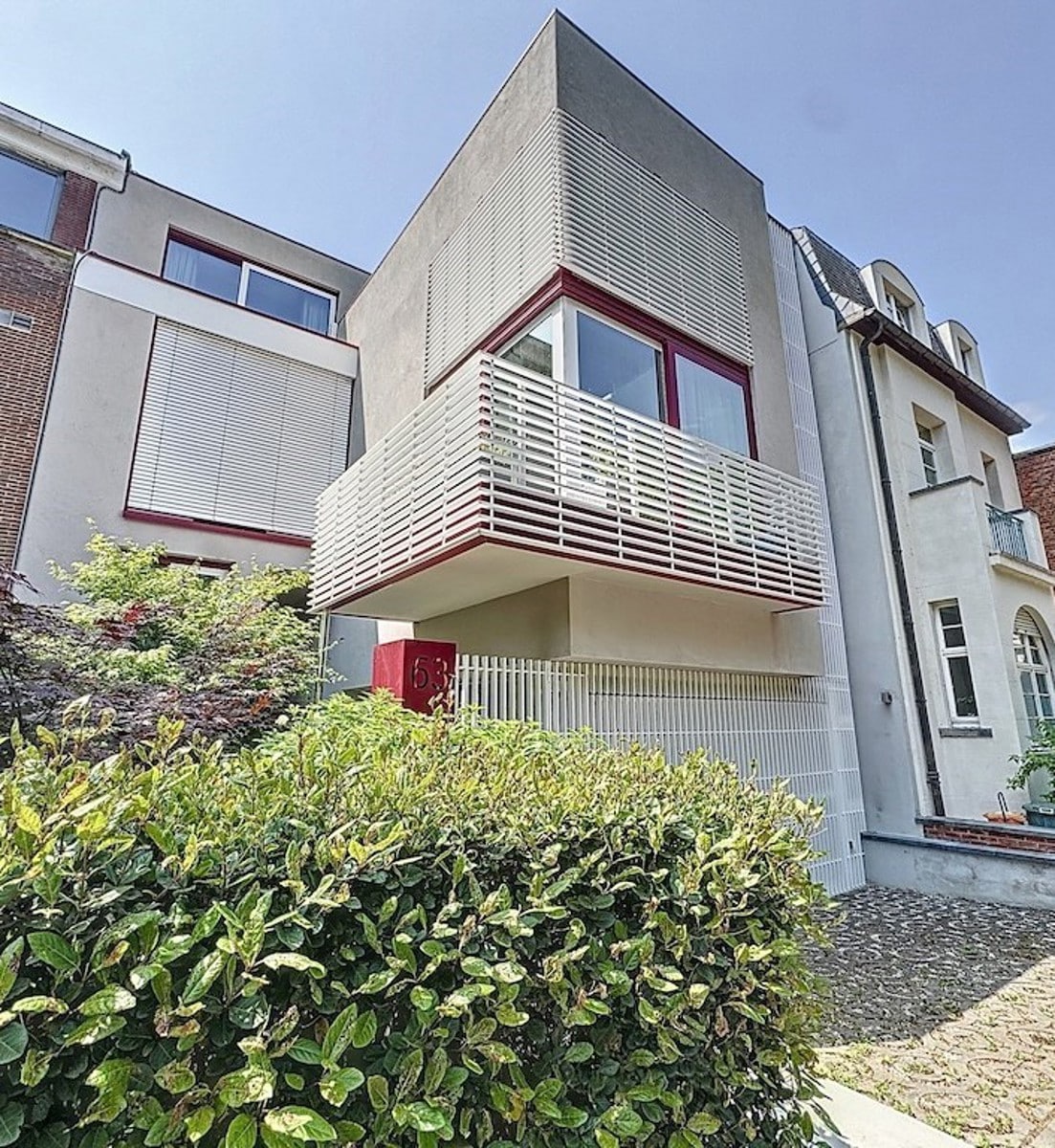 Façade de Maison Contemporaine – You Real Estate Agency Maison contemporaine à façade grise, balcon à lames blanches et fenêtres rouges
