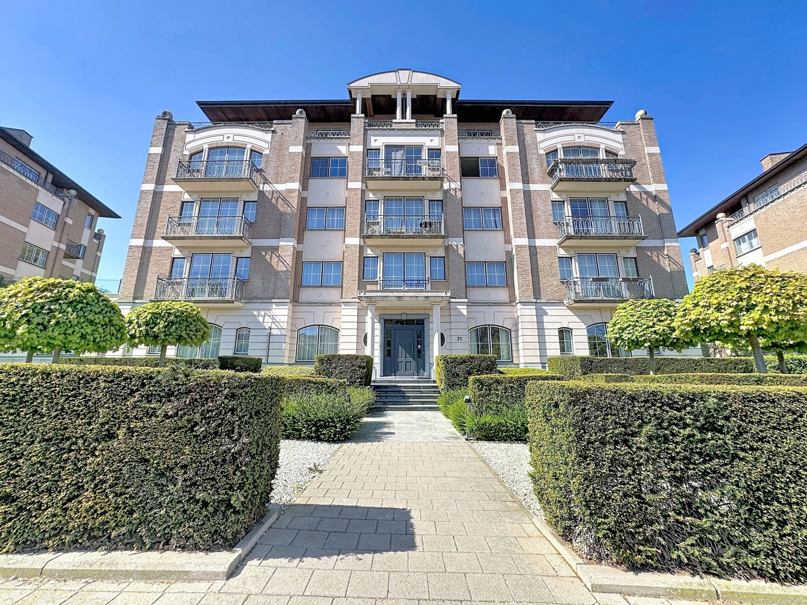 Facade of a brick residence - You Real Estate Agency Brick facade with balconies and landscaped garden