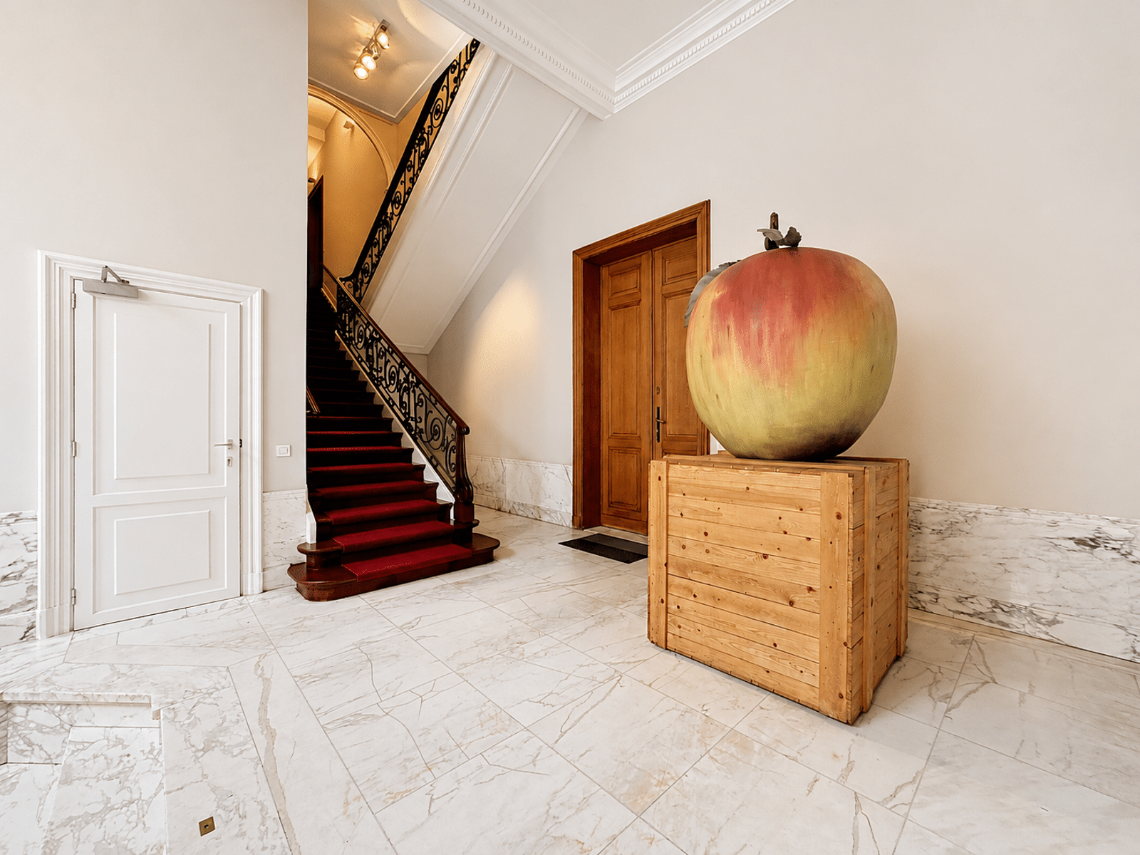 Entrance Hall with Staircase and Apple - You Real Estate Agency Marble entrance hall with red-carpeted staircase and giant apple sculpture
