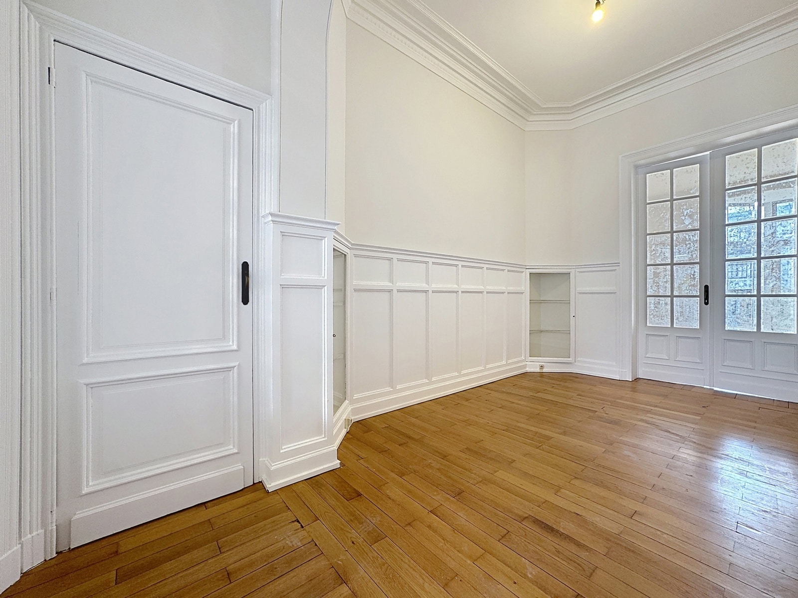 Bright room with wood panelling - You Real Estate Agency Bright room with white woodwork, parquet flooring and classic French windows