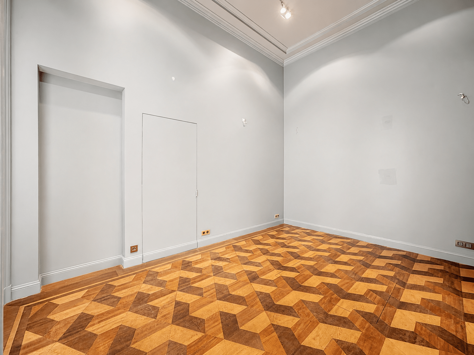 Empty room with geometric parquet - You Real Estate Agency Bright empty room with geometric parquet flooring, elegant mouldings and light grey walls