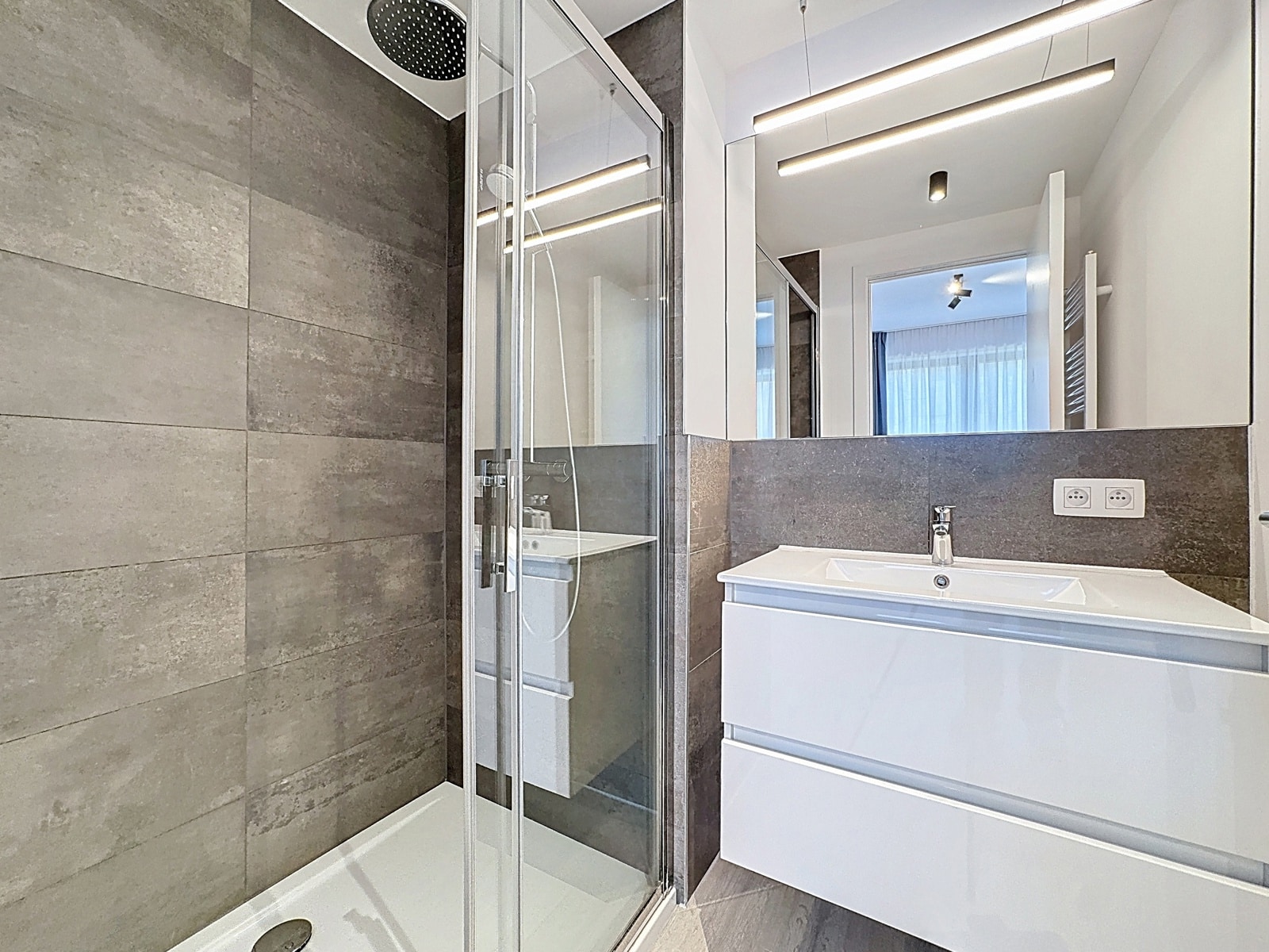 Salle d’Eau Moderne avec Douche Vitrée – You Real Estate Agency Salle de bain moderne avec douche vitrée, carrelage gris et meuble vasque blanc