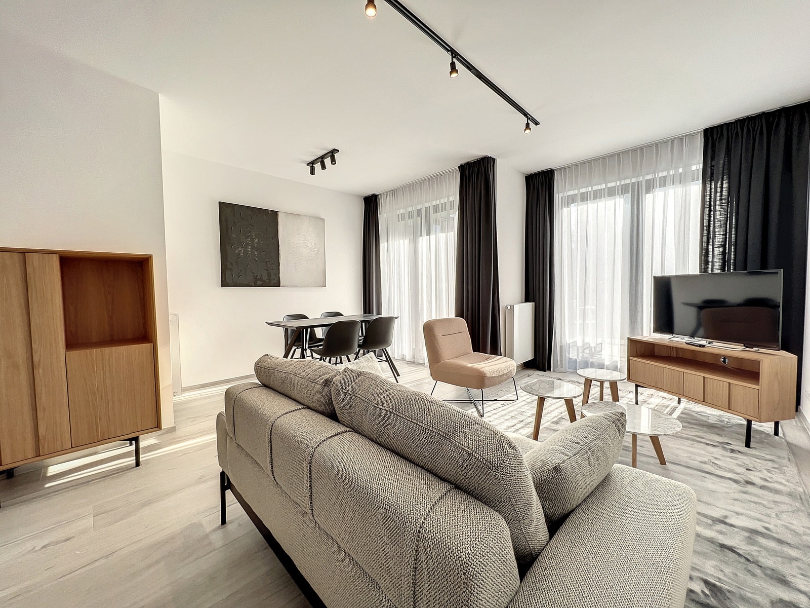Salon Moderne avec Coin Repas – You Real Estate Agency Salon d’appartement moderne et lumineux avec canapé gris, coin repas et grandes fenêtres