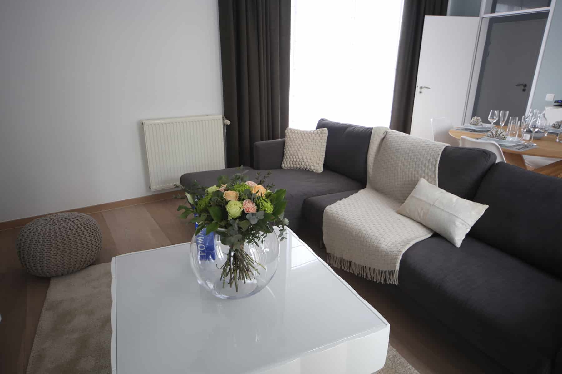 Salon Moderne Lumineux et Coin Repas – You Real Estate Agency Salon moderne lumineux avec canapé gris, table basse fleurie et coin repas élégant
