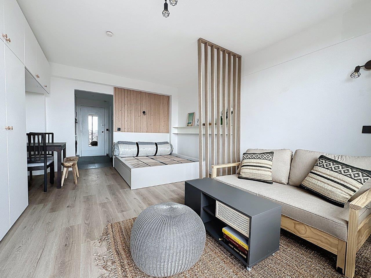 Studio Moderne avec Coin Nuit – You Real Estate Agency Studio moderne lumineux avec salon beige et coin nuit séparé par tasseaux de bois