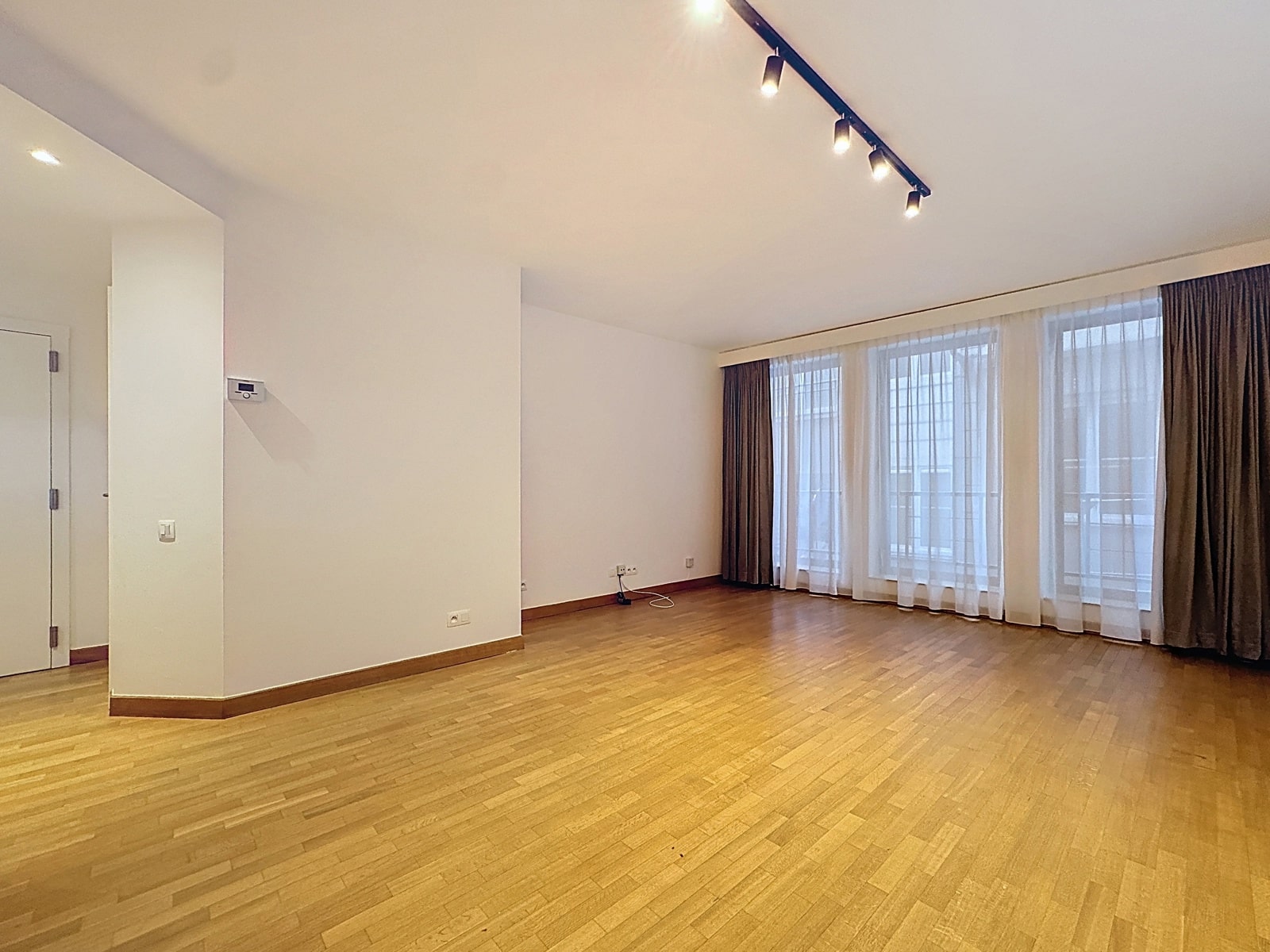 Salon Lumineux avec Baies Vitrées – You Real Estate Agency Salon vide lumineux avec parquet clair, baies vitrées et rideaux voilés