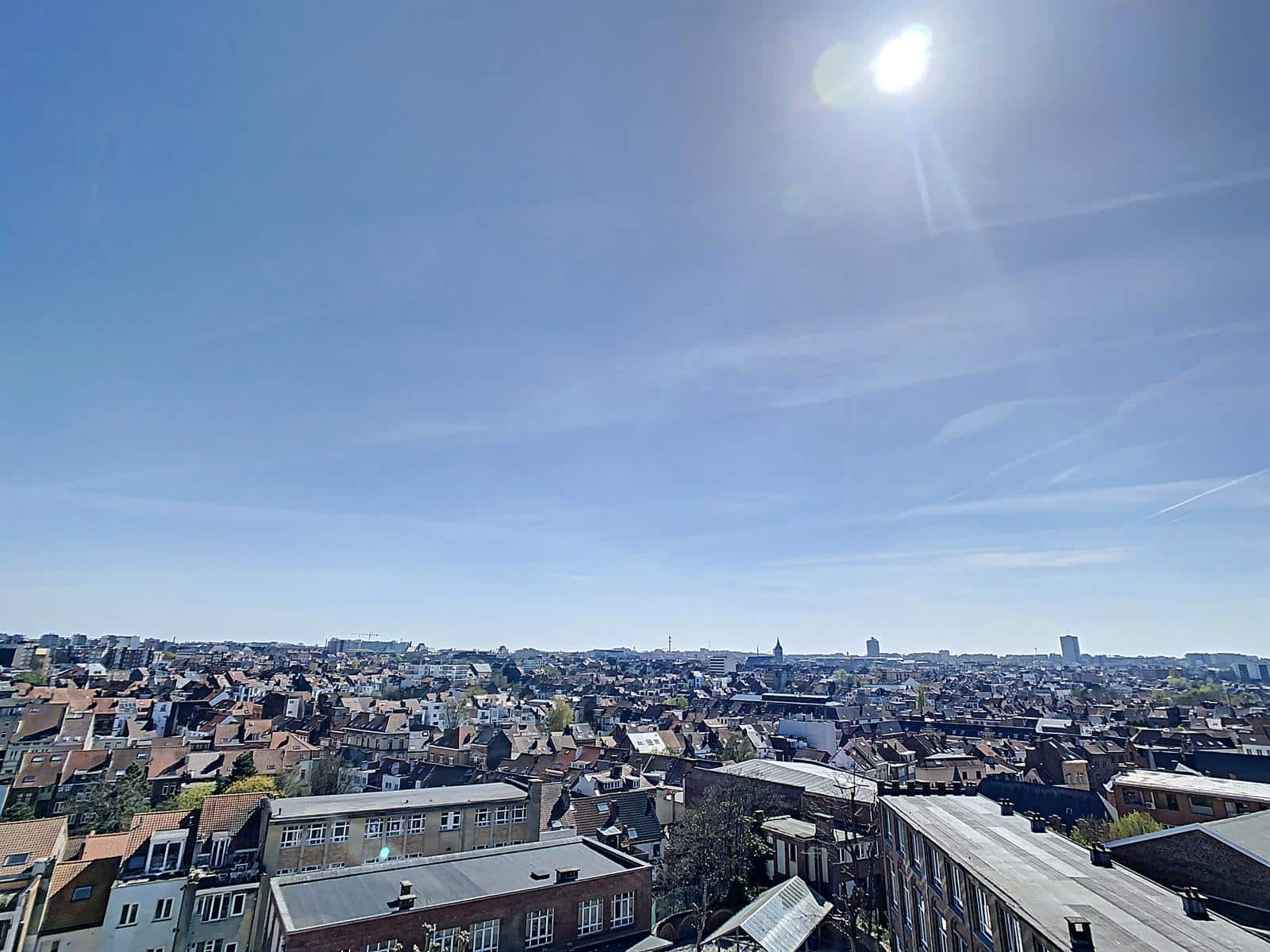 whise photo 5 Wide cityscape view of rooftops under a bright blue sky with the sun high in the corner.