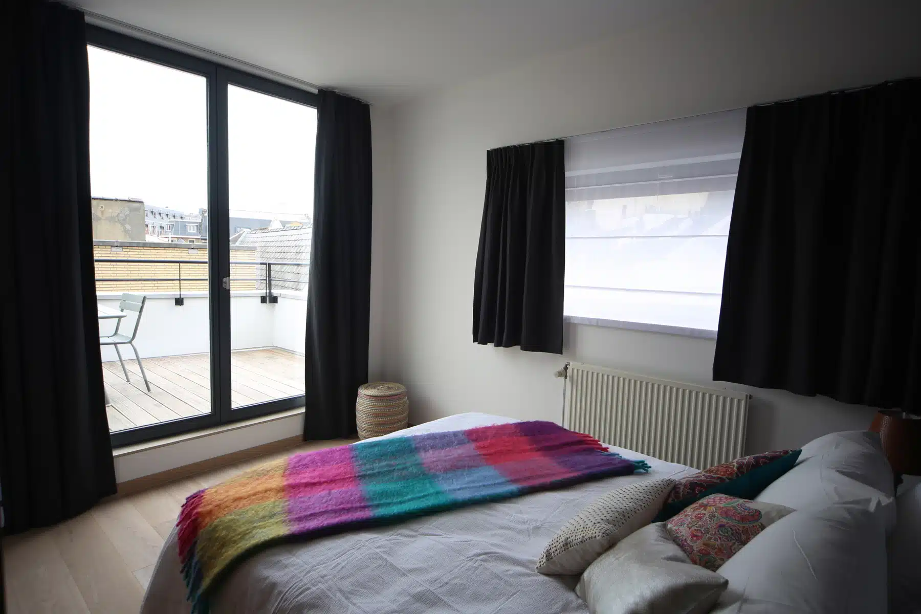 whise photo 10 Bedroom with a large glass door to a wooden balcony; black curtains frame the opening; colorful throw on the bed.