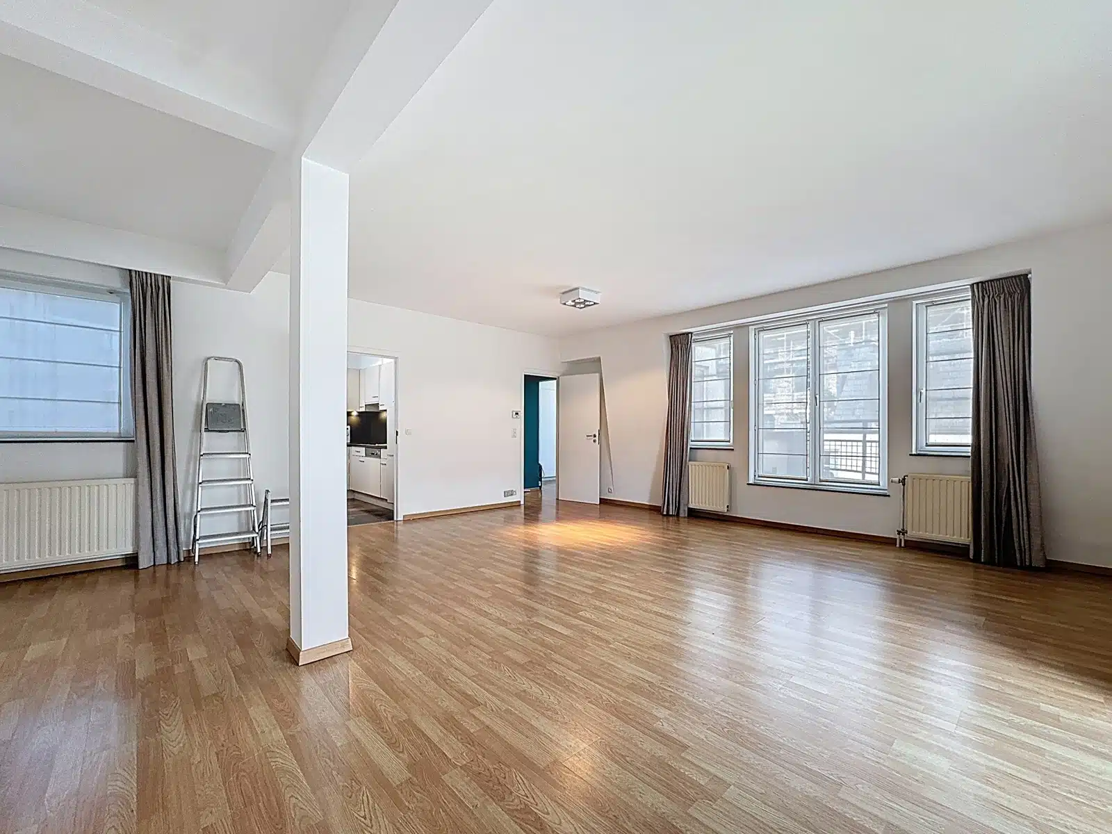 Salon Lumineux Avec Grandes Fenêtres – You Real Estate Agency Salon lumineux d’appartement vide avec parquet, grandes fenêtres et cuisine ouverte.
