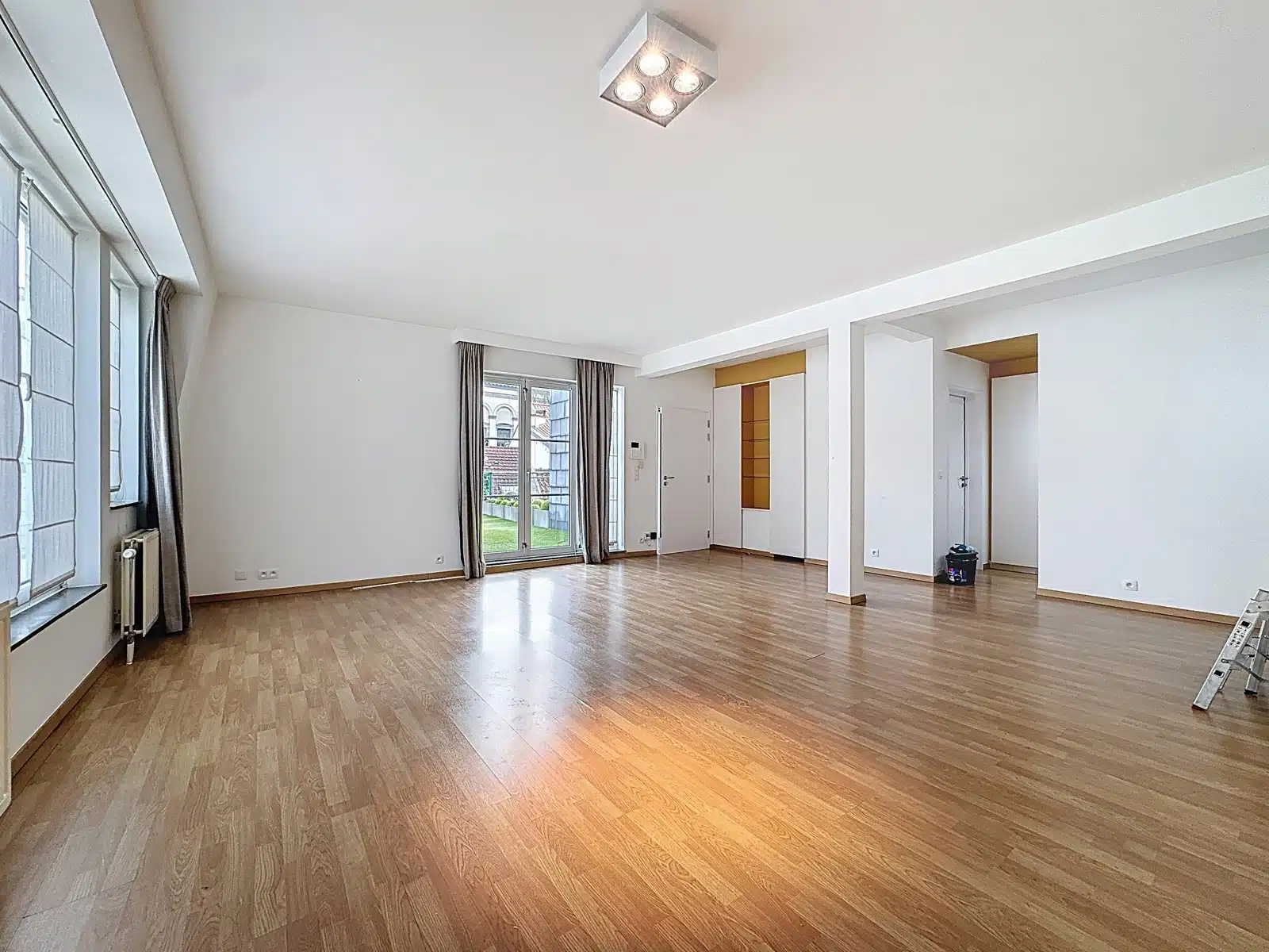 Salon Lumineux avec Accès Jardin – You Real Estate Agency Grand salon lumineux d’appartement avec parquet, baies vitrées et accès jardin.