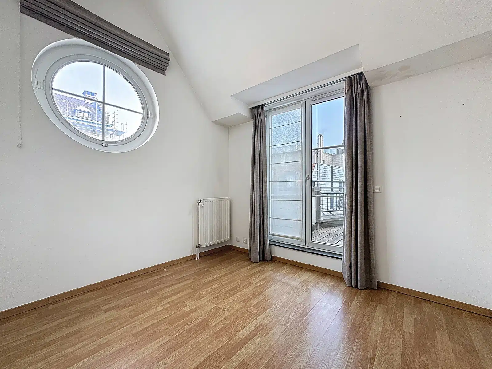 Pièce Lumineuse avec Fenêtre Ronde – You Real Estate Agency Pièce lumineuse d’appartement sous combles avec parquet, fenêtre ronde et terrasse.