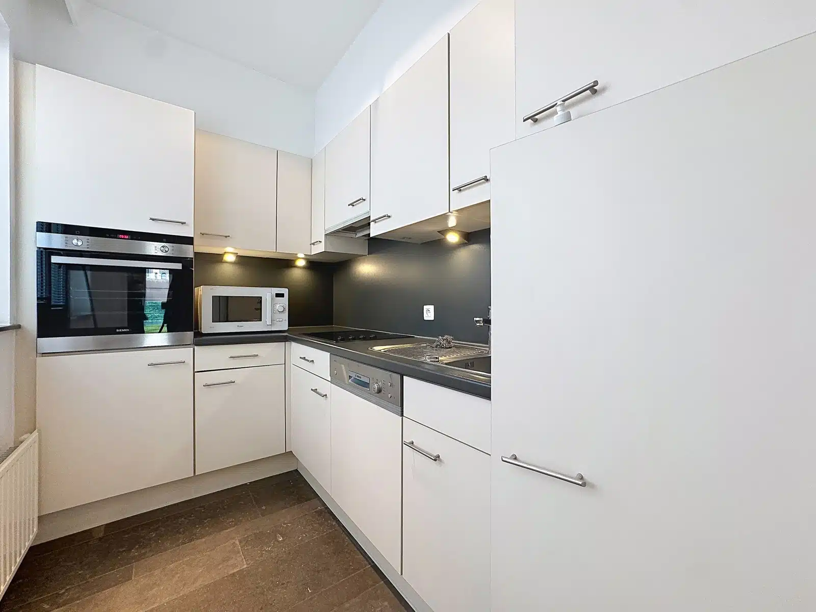 Cuisine Équipée Moderne – You Real Estate Agency Cuisine équipée moderne avec meubles blancs et électroménager intégré.