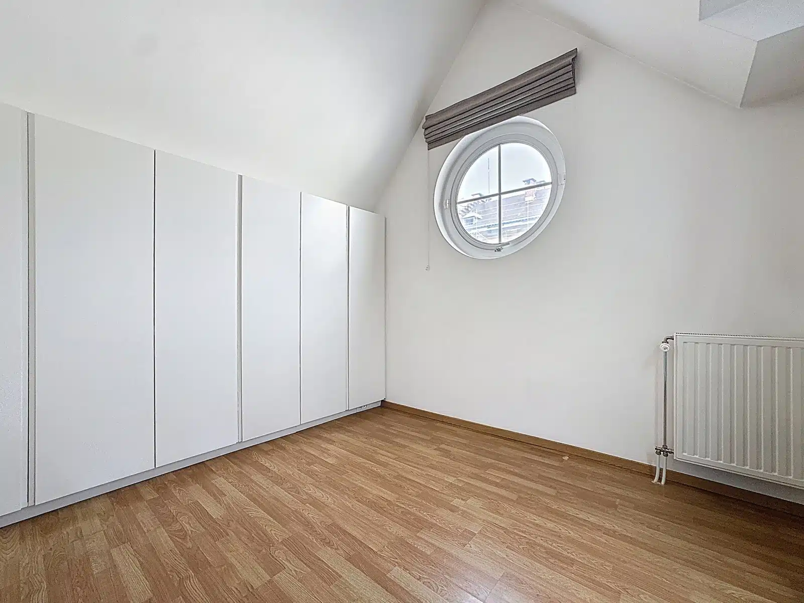 Chambre Mansardée Lumineuse – You Real Estate Agency Chambre mansardée lumineuse d’appartement avec placards intégrés, parquet et fenêtre ronde.