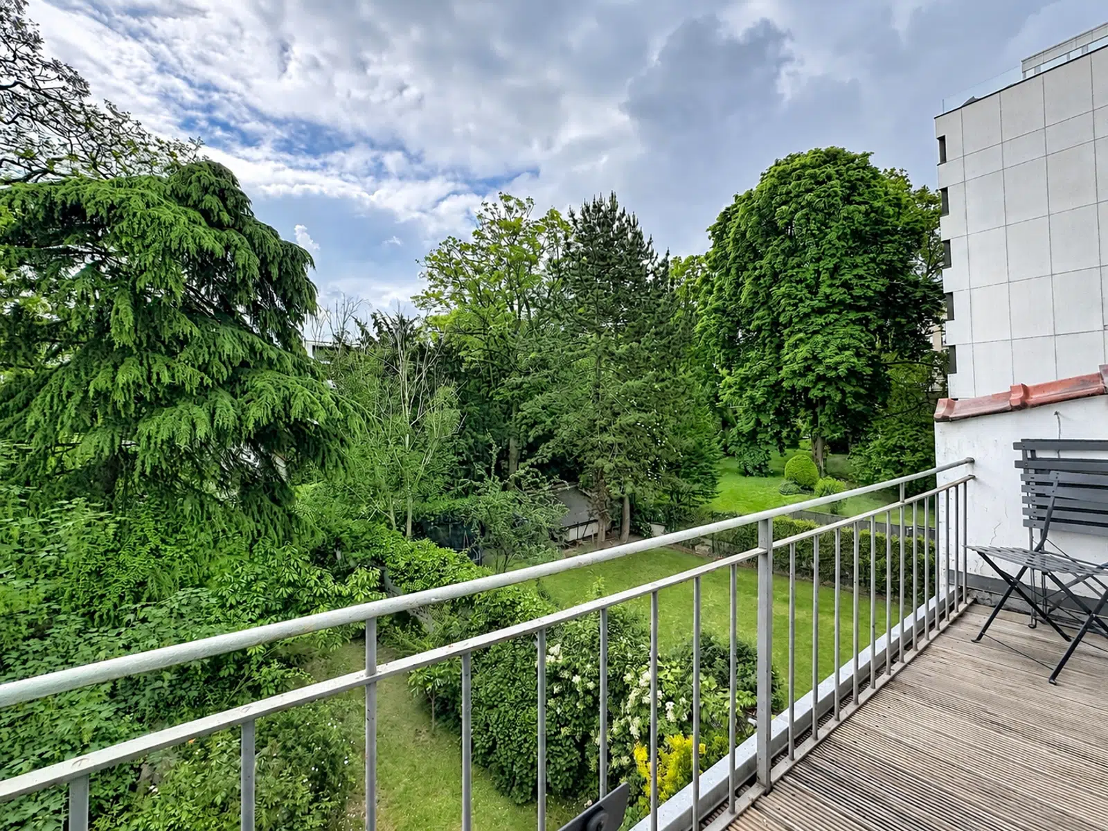 Balcon Avec Vue Sur Jardin Arboré – You Real Estate Agency Terrasse d’appartement avec vue sur jardin arboré et ciel nuageux.