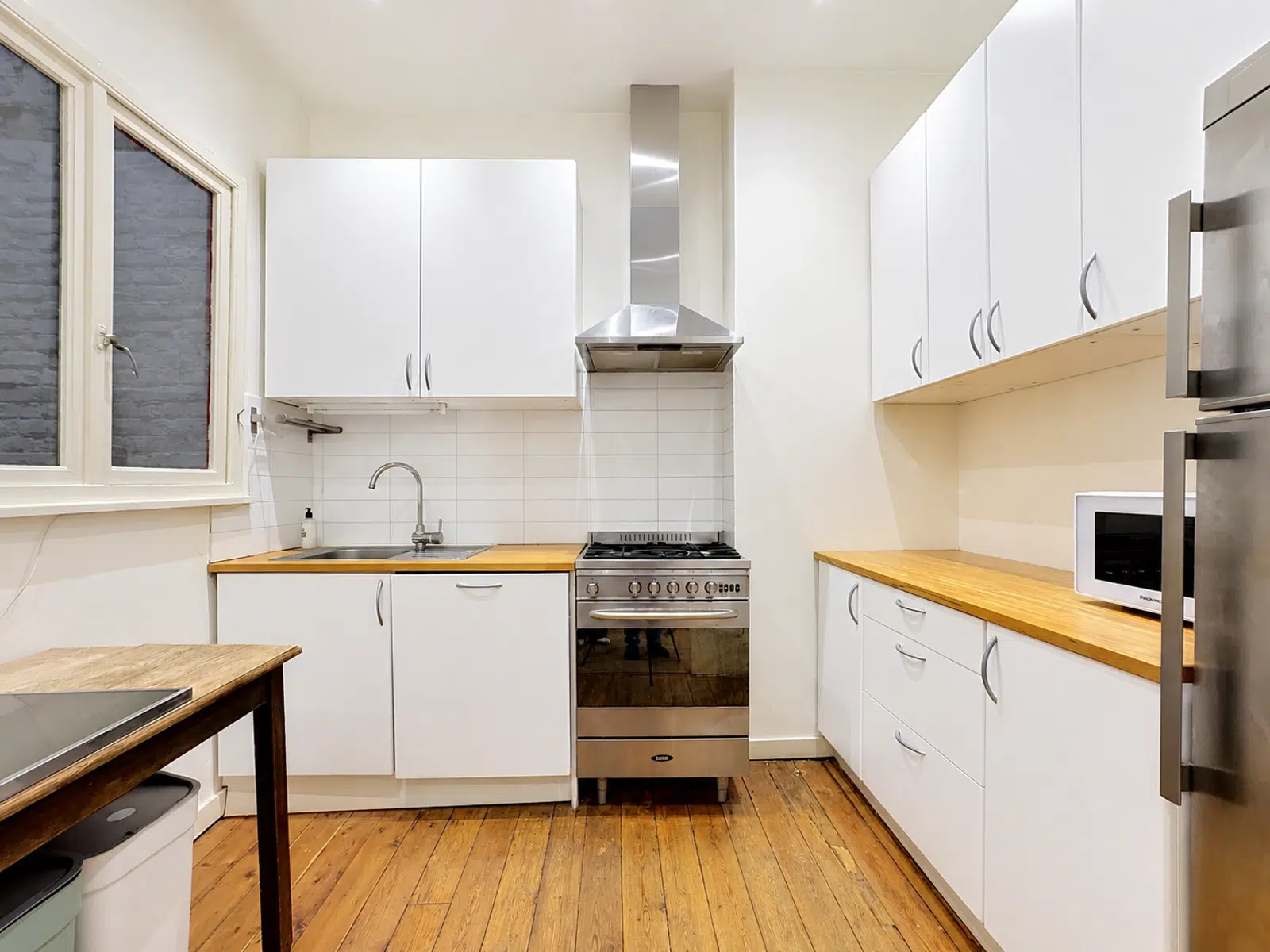 Cuisine Équipée Lumineuse – You Real Estate Agency Cuisine équipée lumineuse avec meubles blancs, plan de travail bois et électroménager inox.