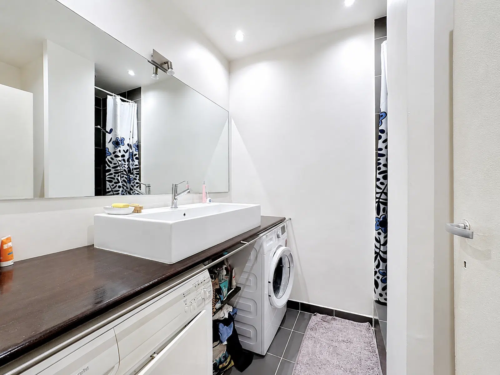 Salle de Bains Moderne avec Buanderie – You Real Estate Agency Salle de bains moderne avec buanderie intégrée et grande vasque en appartement.