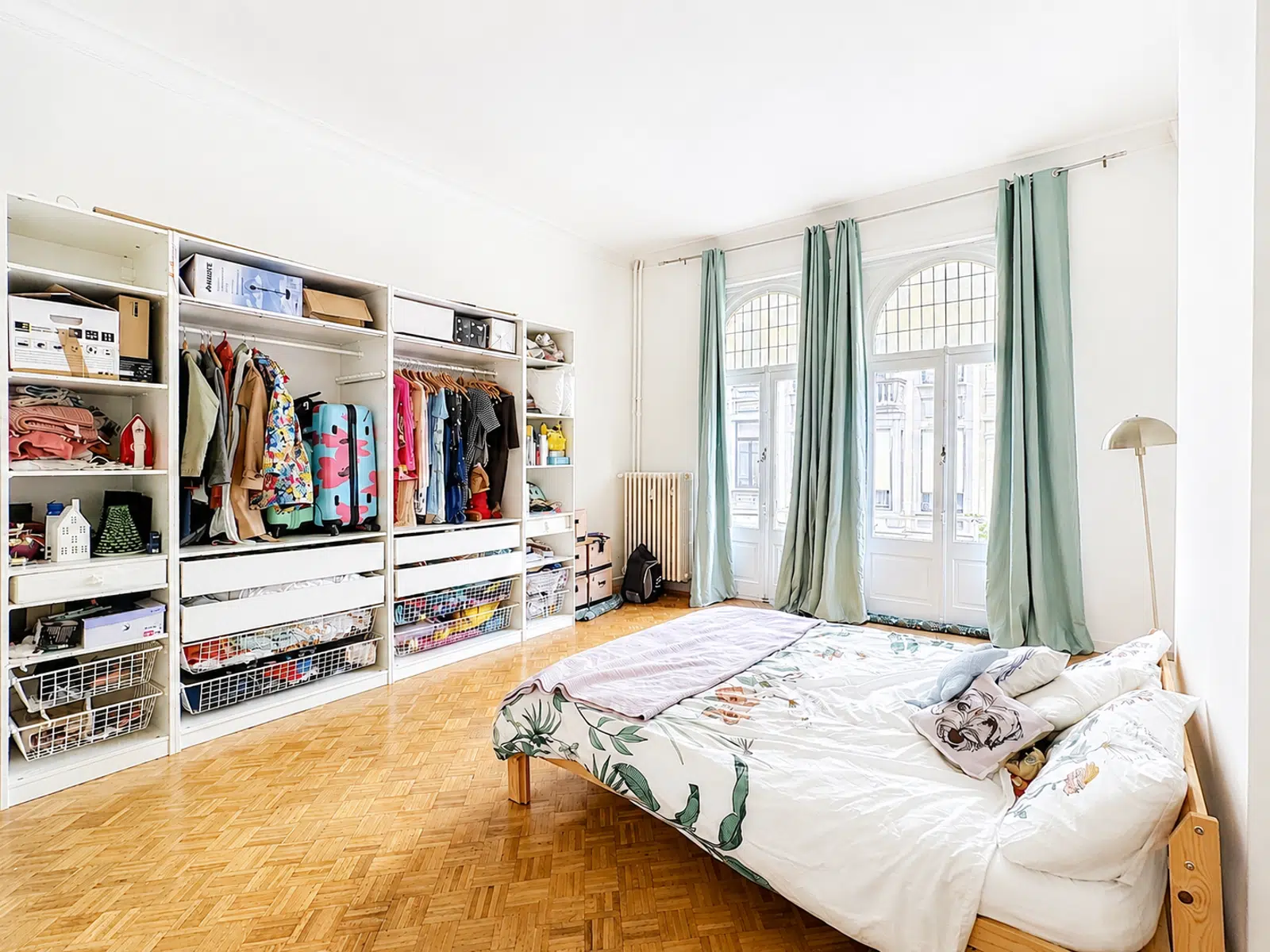 Chambre Lumineuse avec Dressing Ouvert – You Real Estate Agency Chambre lumineuse d’appartement avec dressing ouvert, parquet et grandes fenêtres arquées.