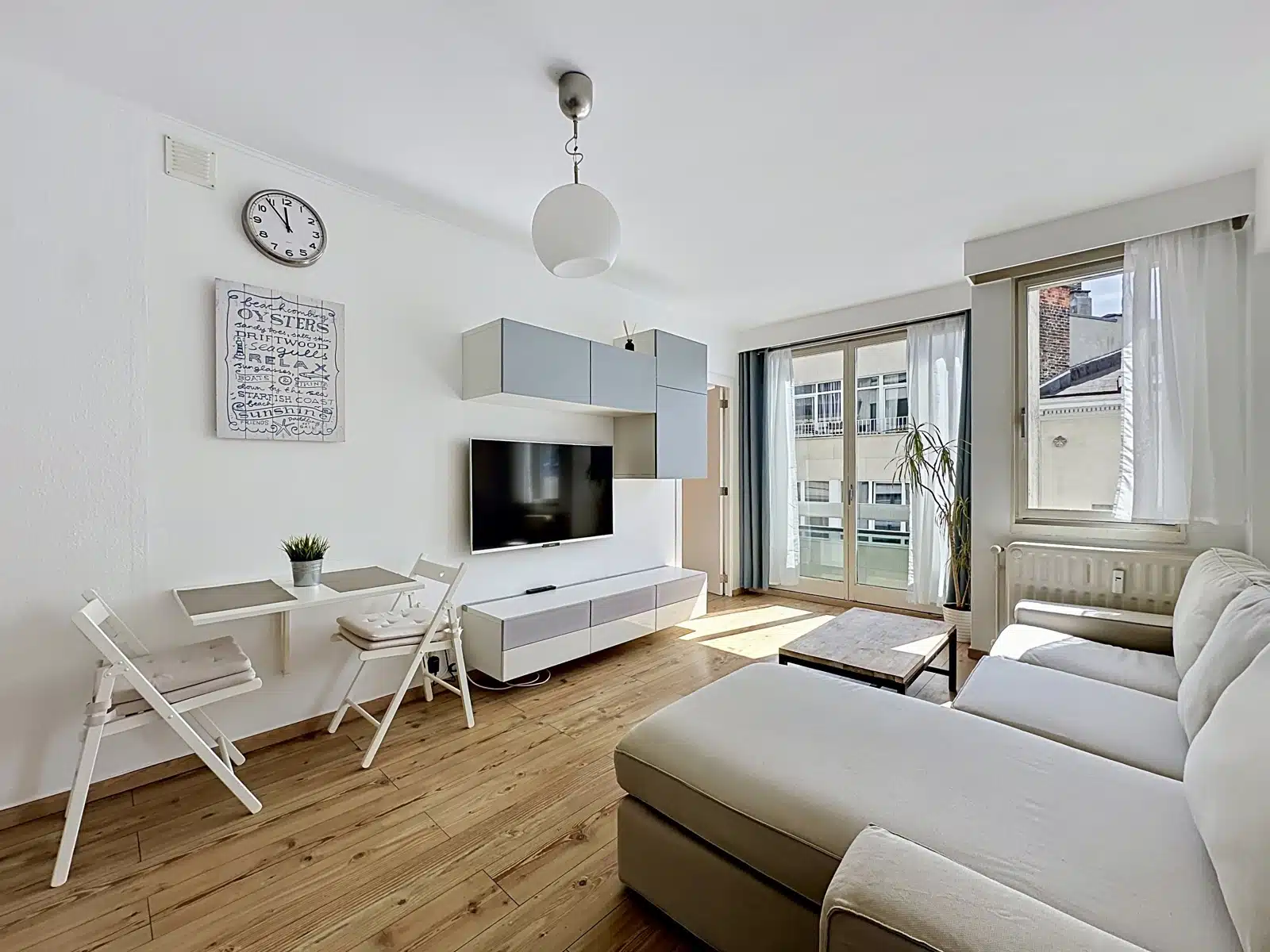 whise photo 2 Bright living room with white walls, wall clock, TV on a low console, and blue-gray wall cabinets above.